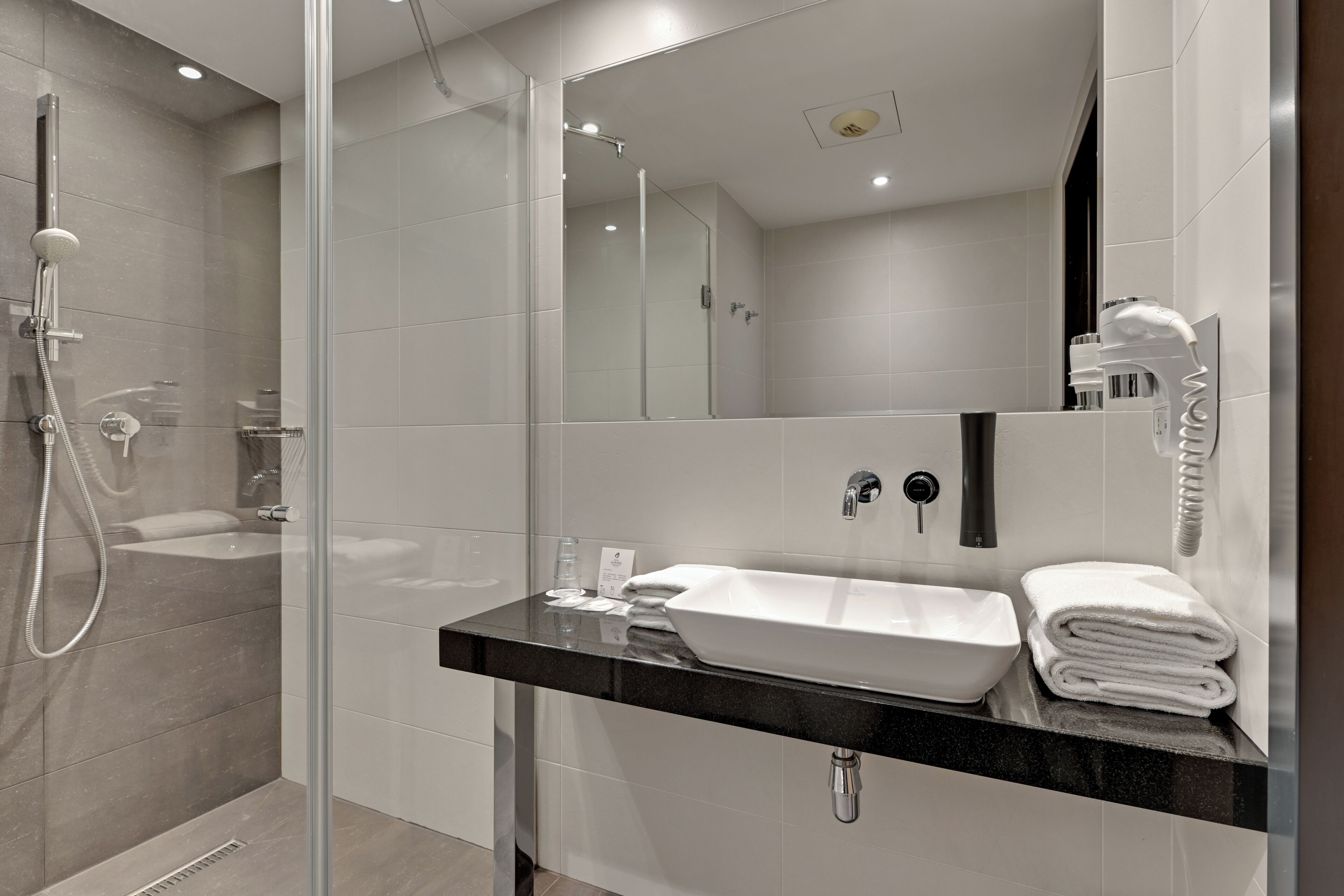 A modern bathroom with a glass-enclosed shower, a black countertop sink, and a mirror.