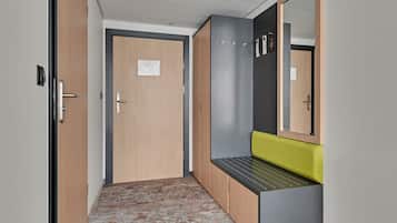 A hallway with a wooden door, a grey bench with a green cushion, and a mirror on the wall.