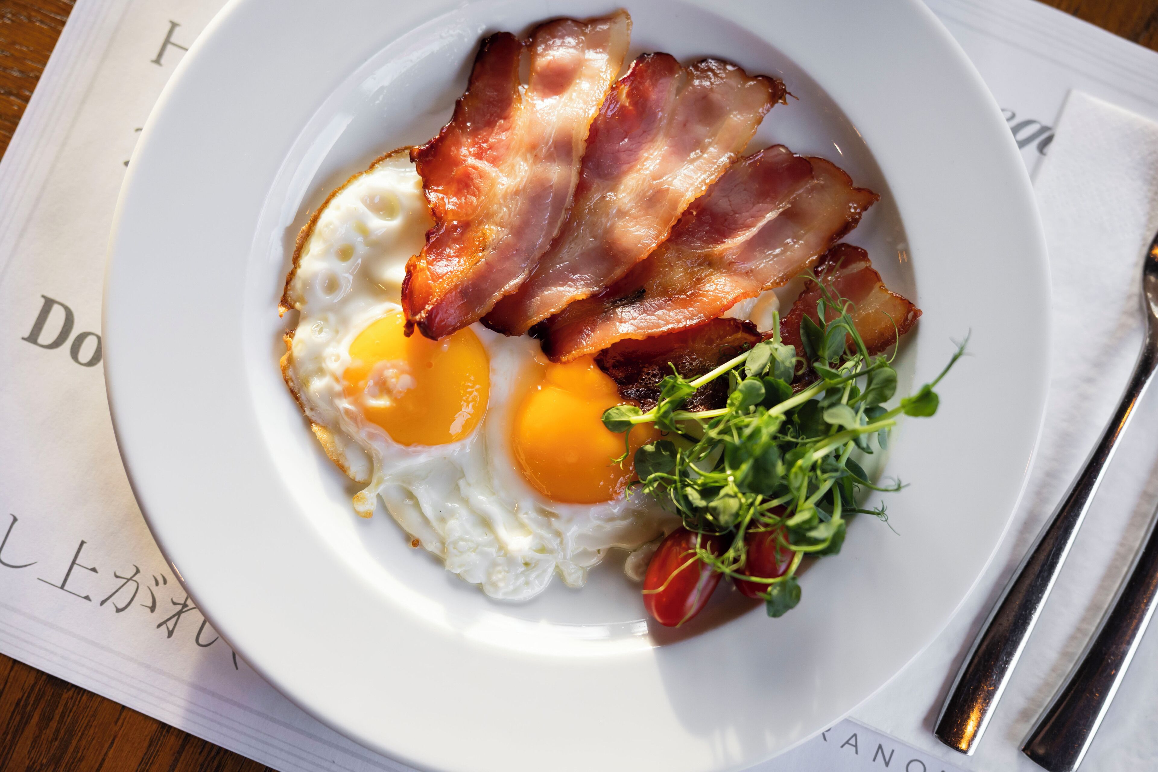 A plate with eggs, bacon, and greens on a white plate.