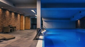 A modern indoor swimming pool with a blue tiled floor, surrounded by brick walls and wooden paneling. - Grano Hotel**** Gdańsk Riverside (Gdansk)