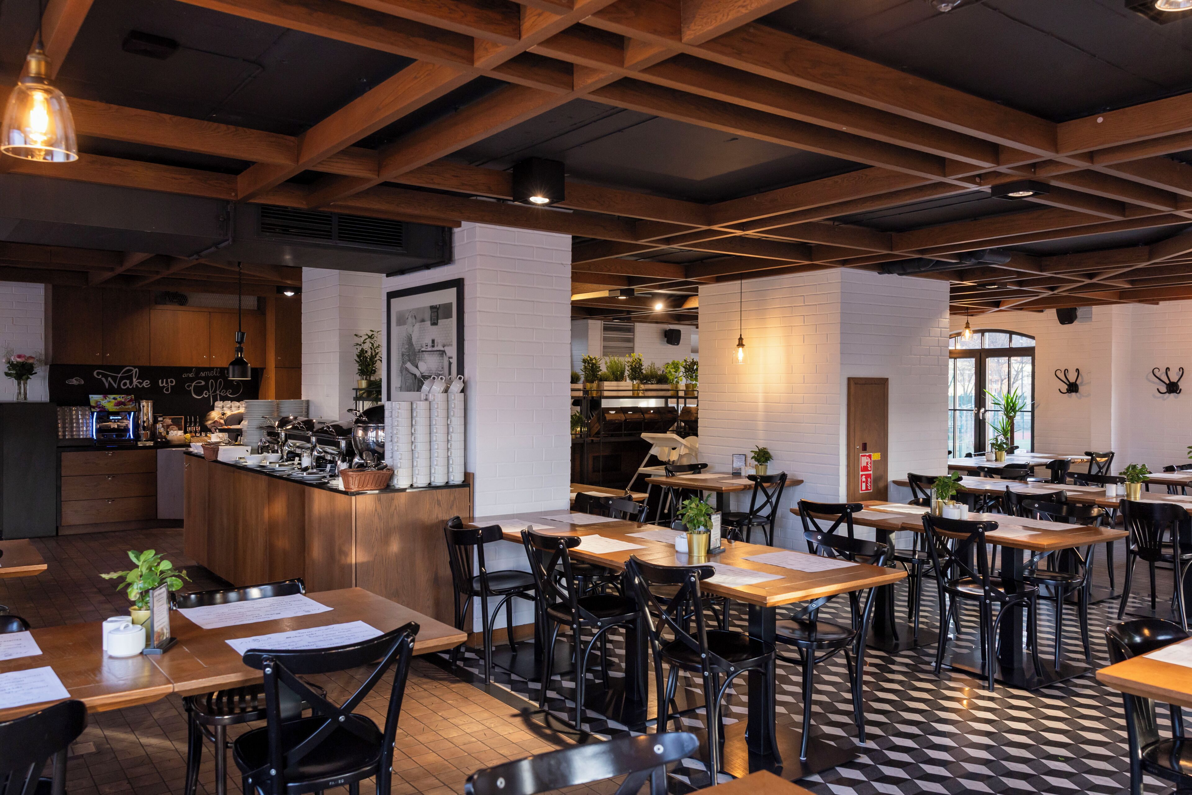 Un interior de restaurante con vigas de madera, suelo a cuadros blanco y negro, y varias mesas y sillas.