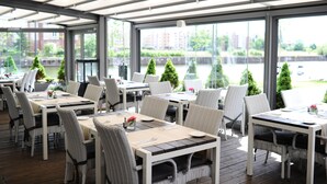 An outdoor dining area with tables and chairs, large windows, and greenery outside. - Grano Hotel**** Gdańsk Riverside (Gdansk)