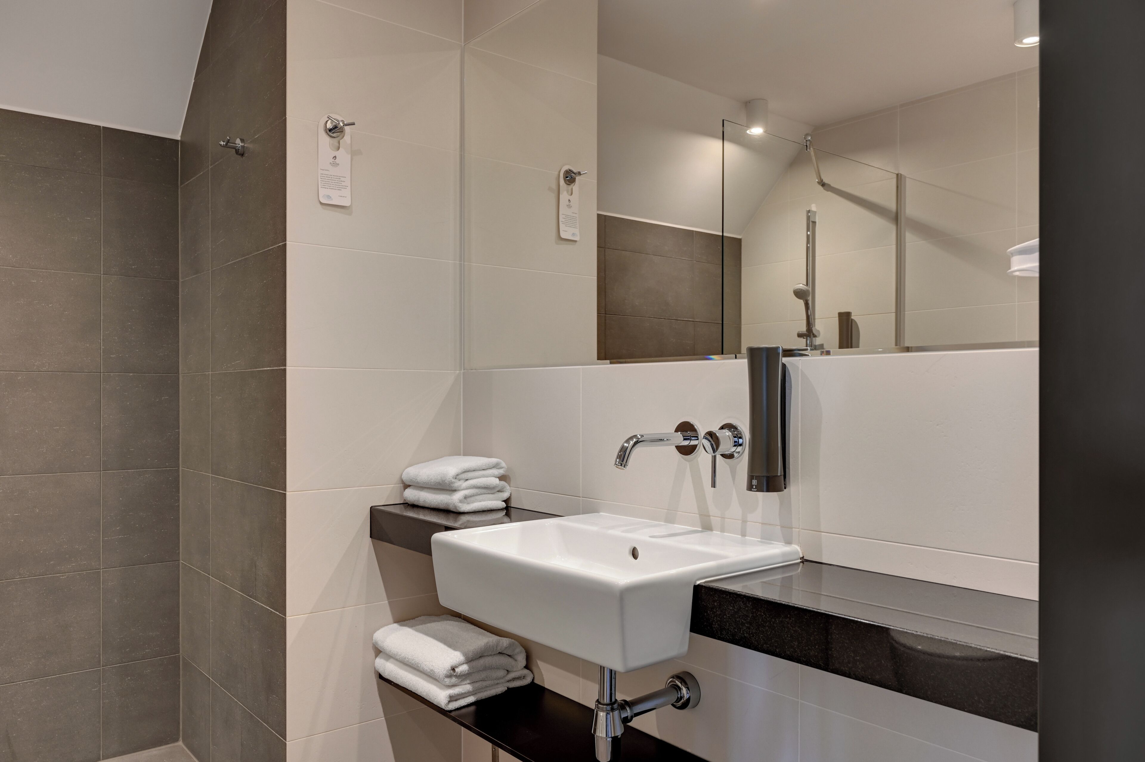 A modern bathroom with a white sink, a mirror, and a shower area.