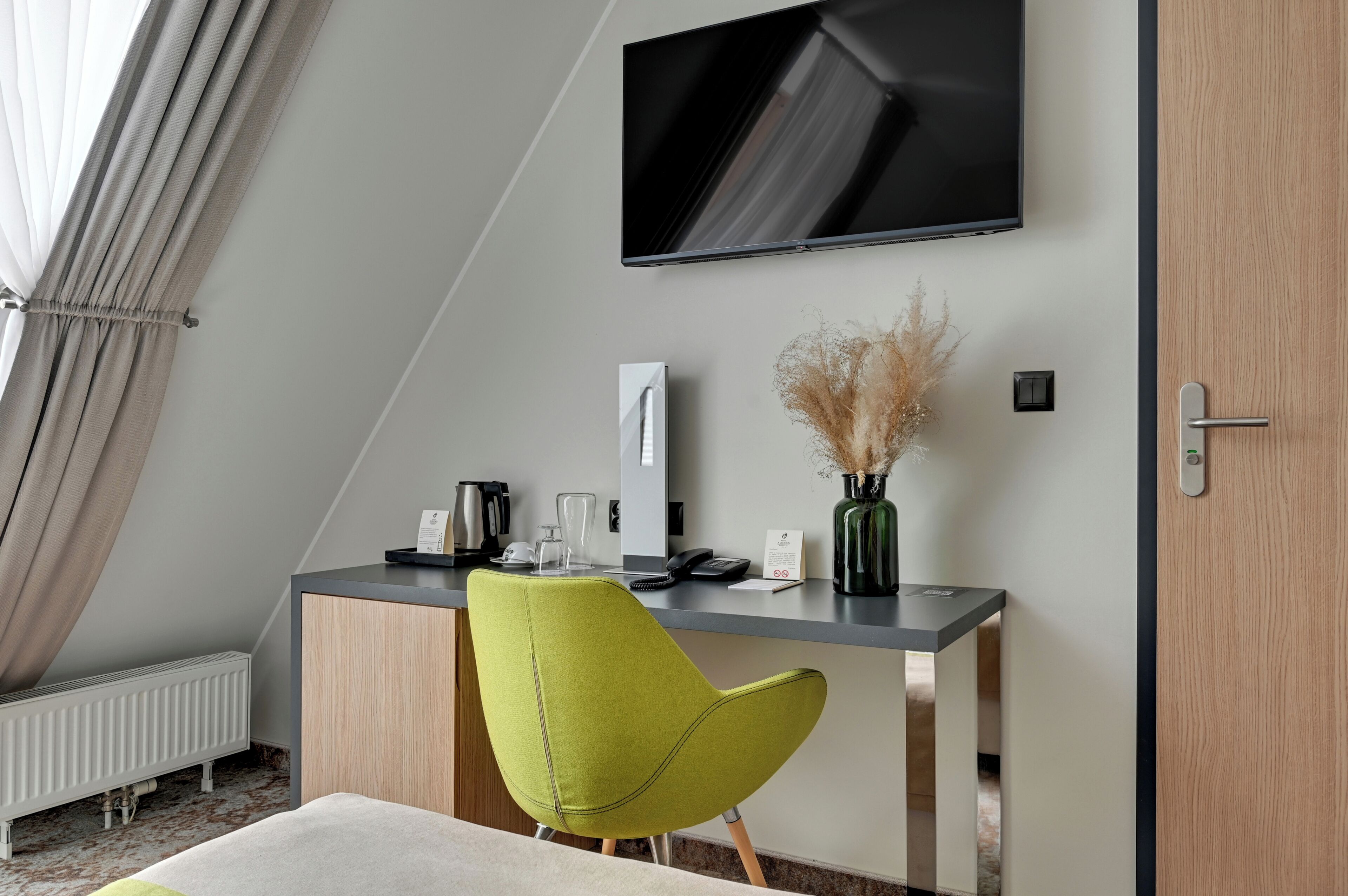 Ein modernes Hotelzimmer mit Schreibtisch, Stuhl, Flachbildfernseher und Heizkörper.