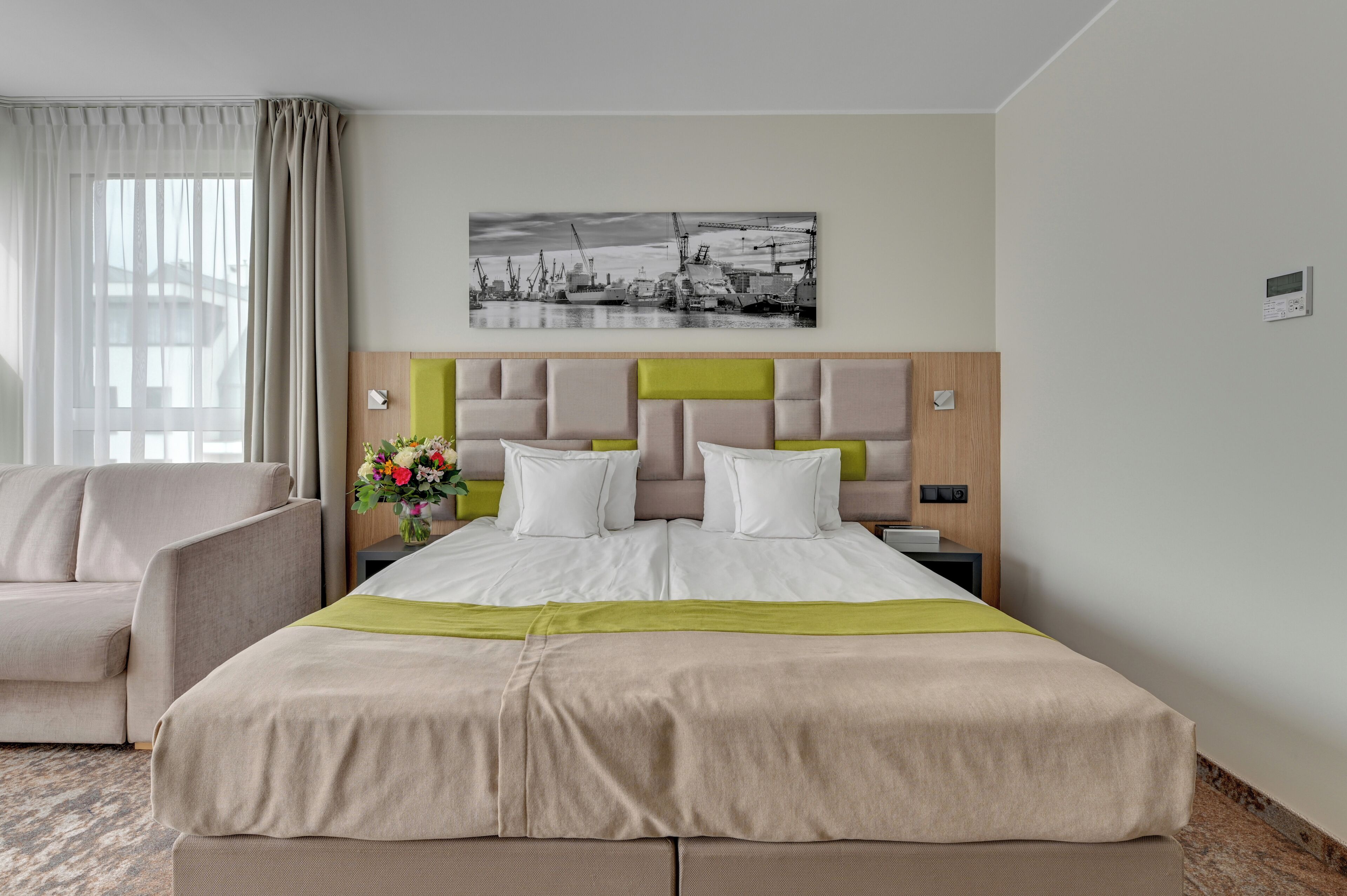 A hotel room with a bed, a chair, a nightstand, a picture on the wall, and a window with curtains.