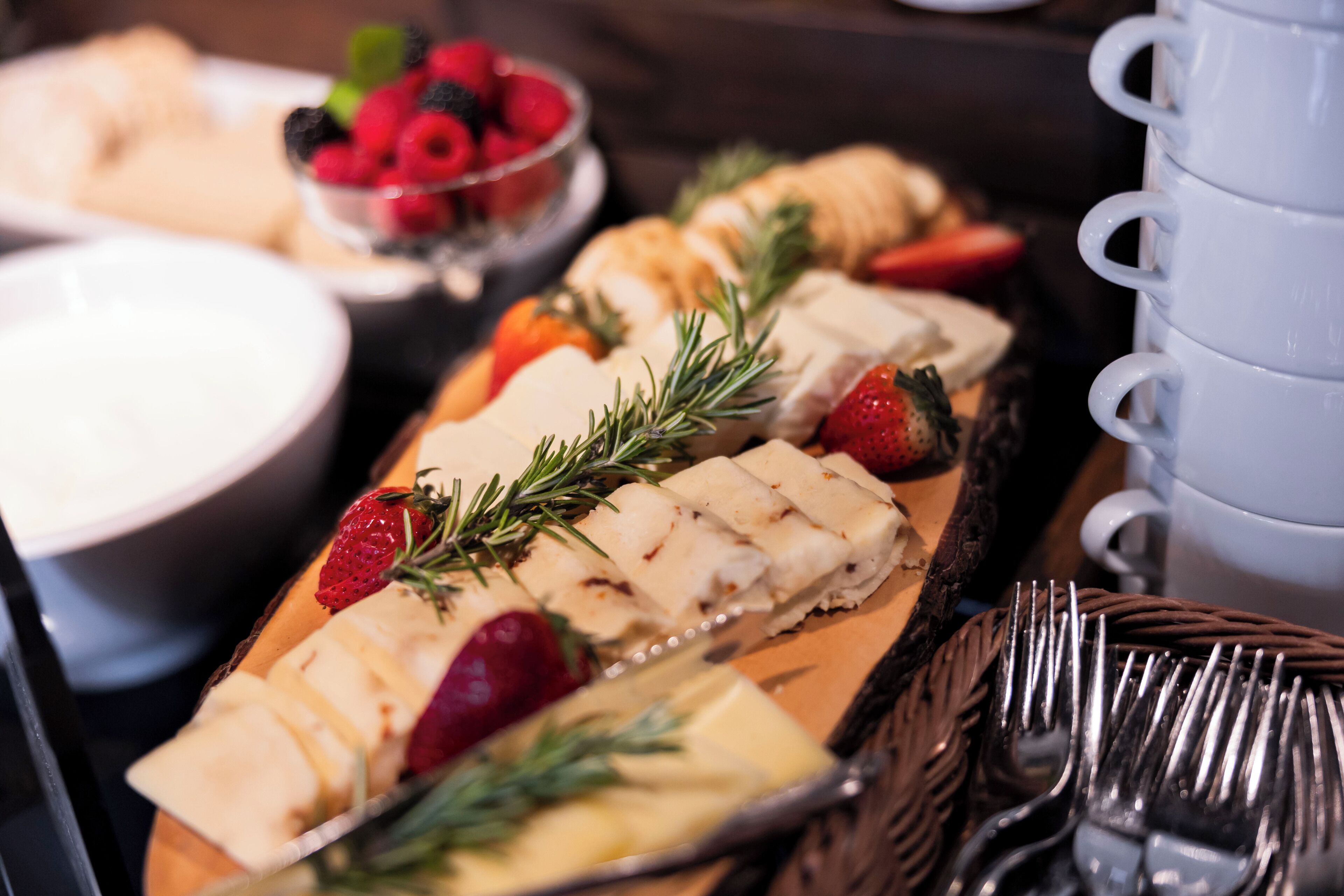 A tray of food with sliced cheese, strawberries, and a sprig of rosemary.
