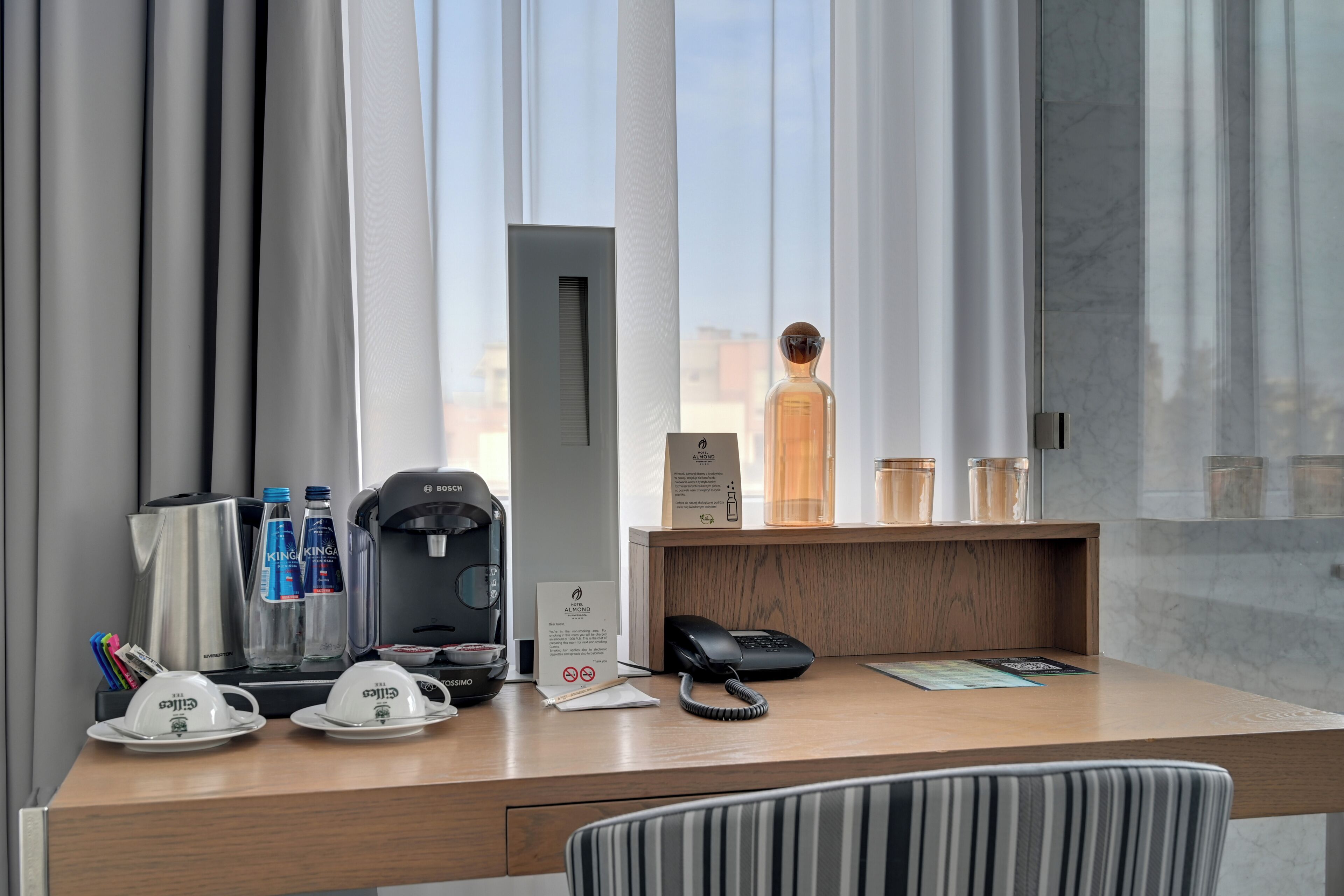 Escritorio de hotel con cafetera, botellas de agua, teléfono y un cartel.