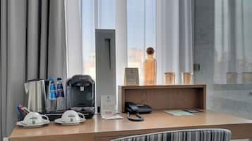 Escritorio de hotel con cafetera, botellas de agua, teléfono y un cartel.