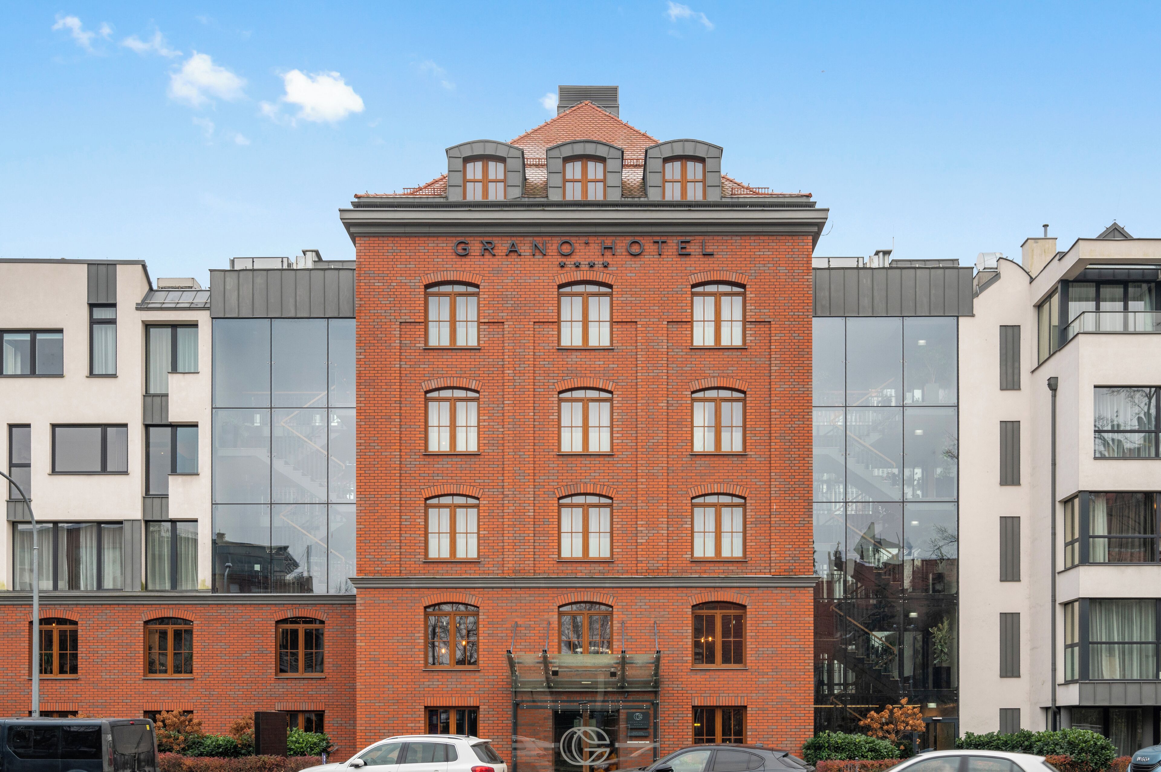 Een gebouw van baksteen met het bord 'GRANO HOTEL' en grote ramen.