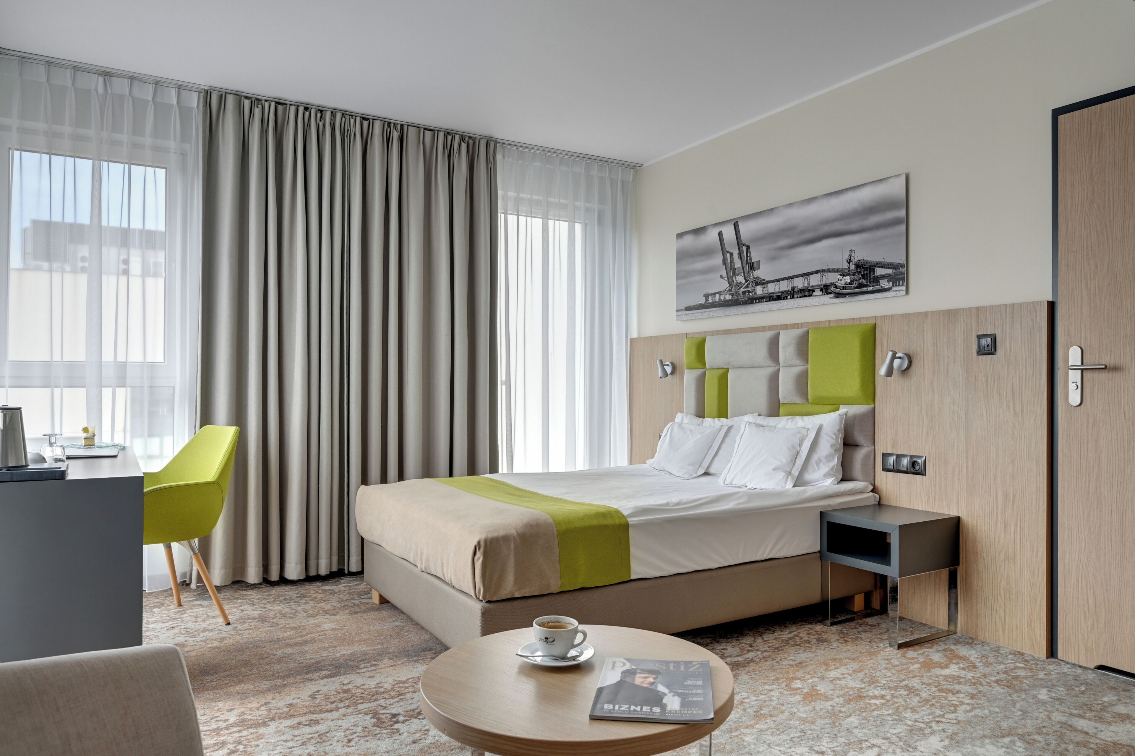 A hotel room with a bed, a desk, a chair, a coffee table, and a painting on the wall.