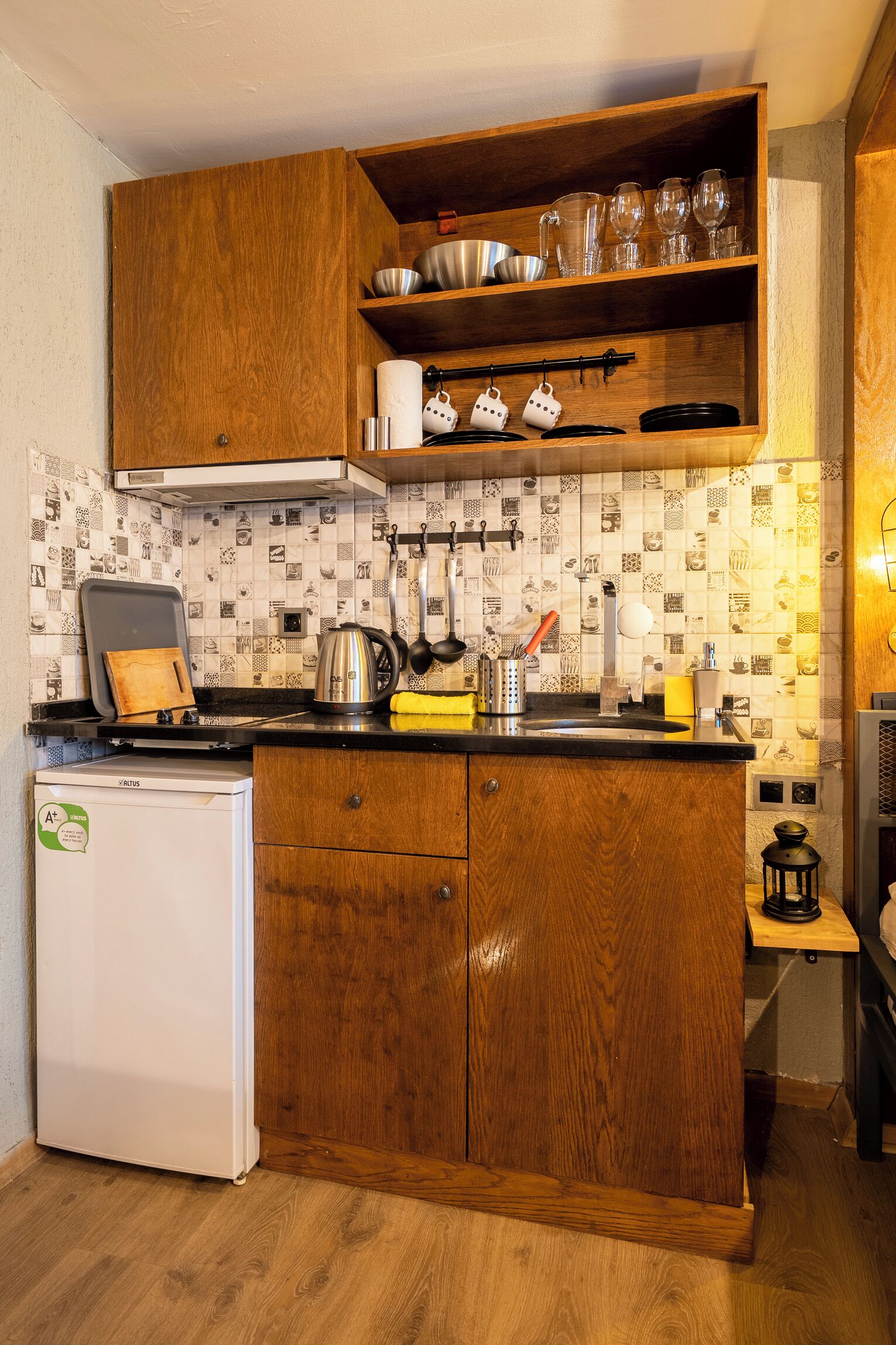 Une cuisine compacte avec des meubles en bois, un petit réfrigérateur et un pare-feu en carreaux.