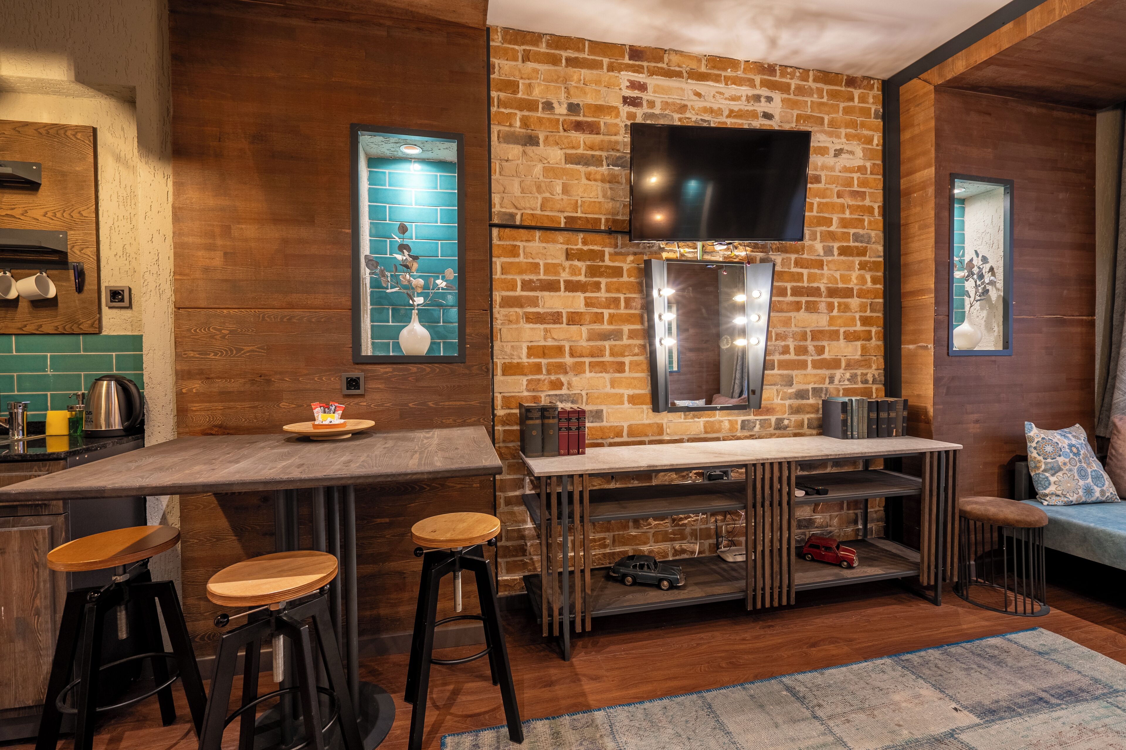 A modern kitchen with a brick wall, a flat-screen TV, and a bar area with stools.