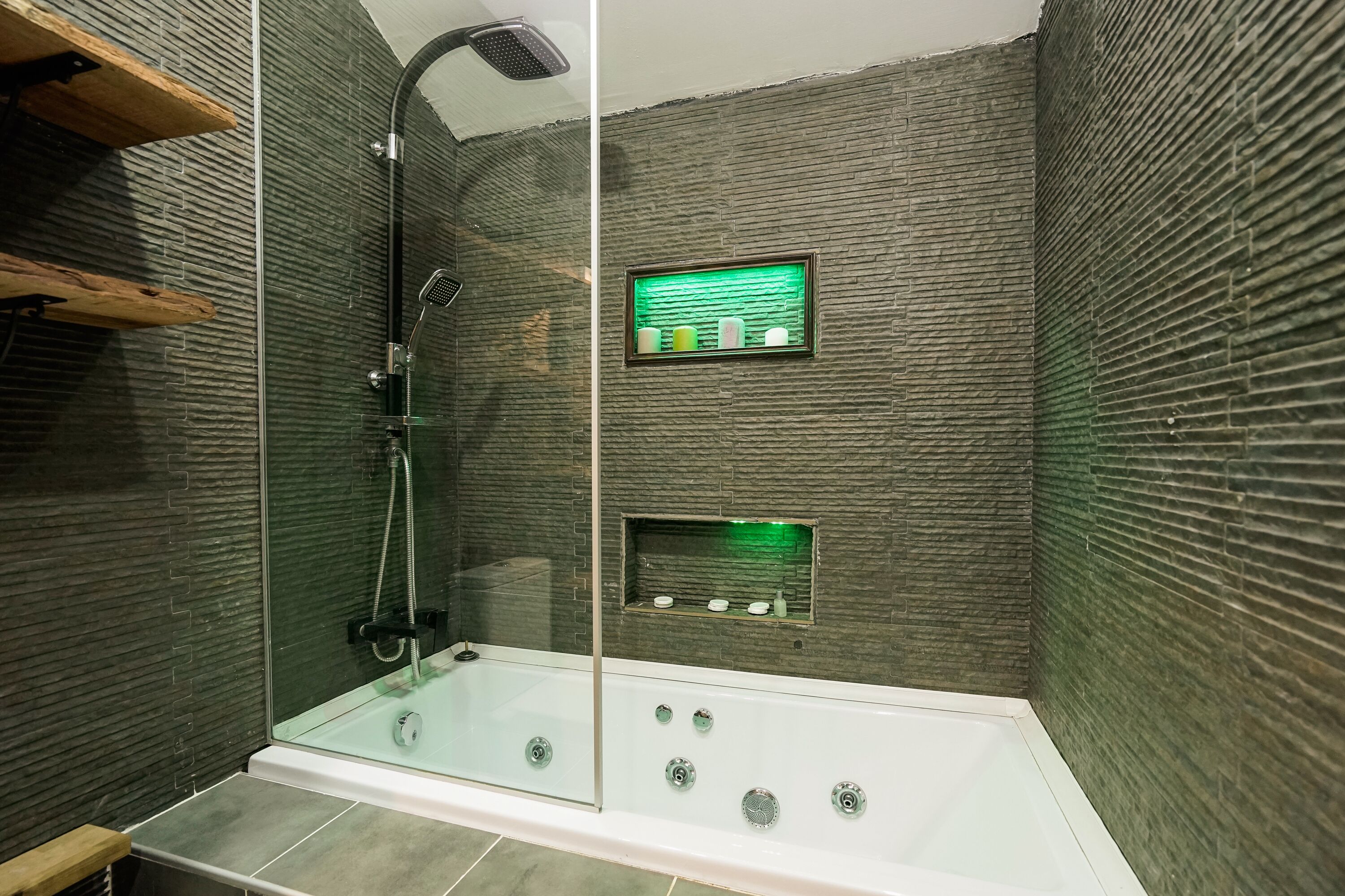 A modern shower with a glass enclosure, a handheld showerhead, and a control panel with a green-lit display.