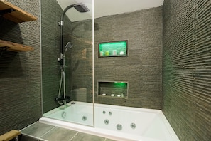 A modern shower with a glass enclosure, a handheld showerhead, and a control panel with a green-lit display.