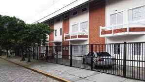 A residential building with a brick facade, white windows, and a black metal fence. - Flat H Ubatuba (Ubatuba)