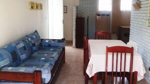 A living room with a sofa, a dining table with chairs, a fireplace, and a kitchen area. - Flat H Ubatuba (Ubatuba)