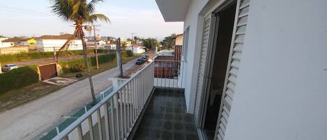 A balcony with a view of a street, palm trees, and a building with a white facade.