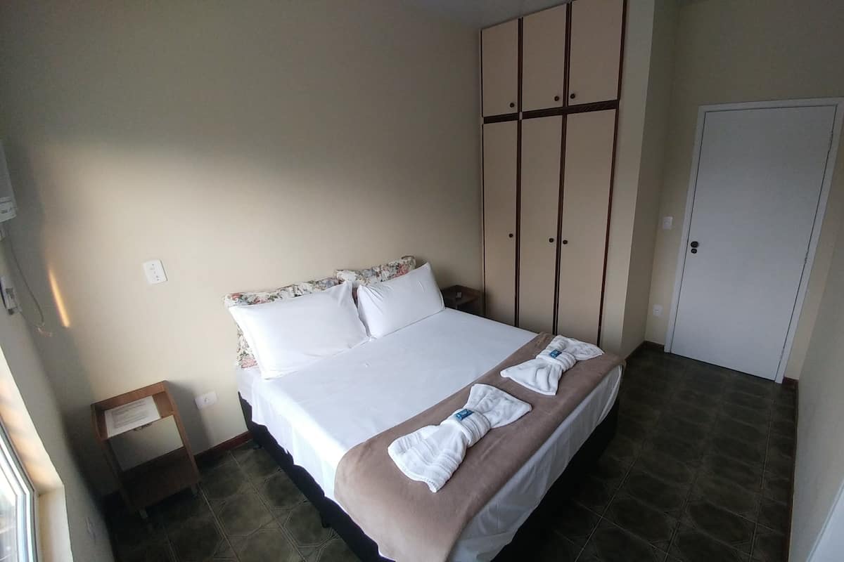 A hotel room with a bed, a wardrobe, a bedside table, and a door.
