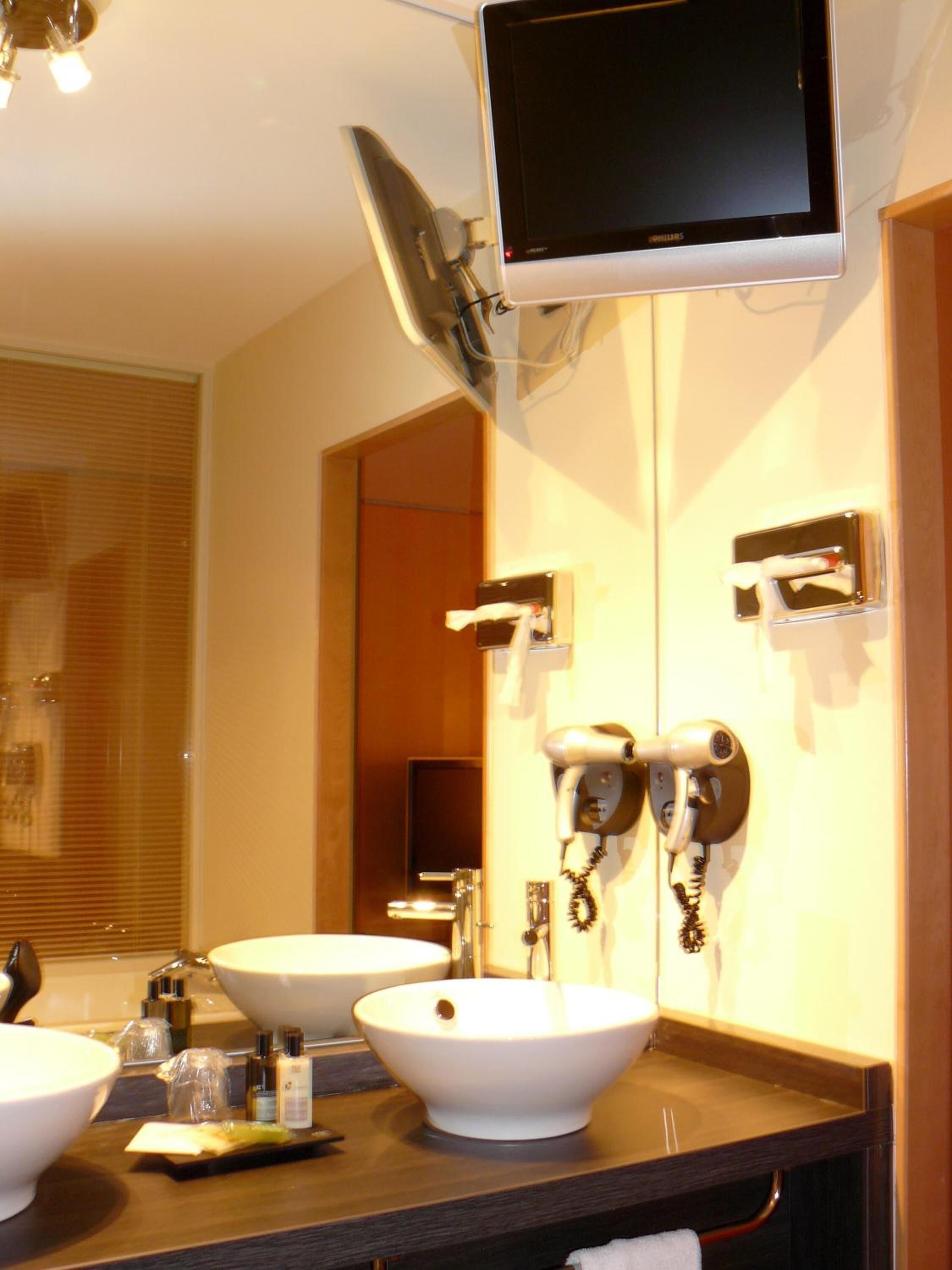 A bathroom with two sinks, a hairdryer, and a television mounted on the wall.