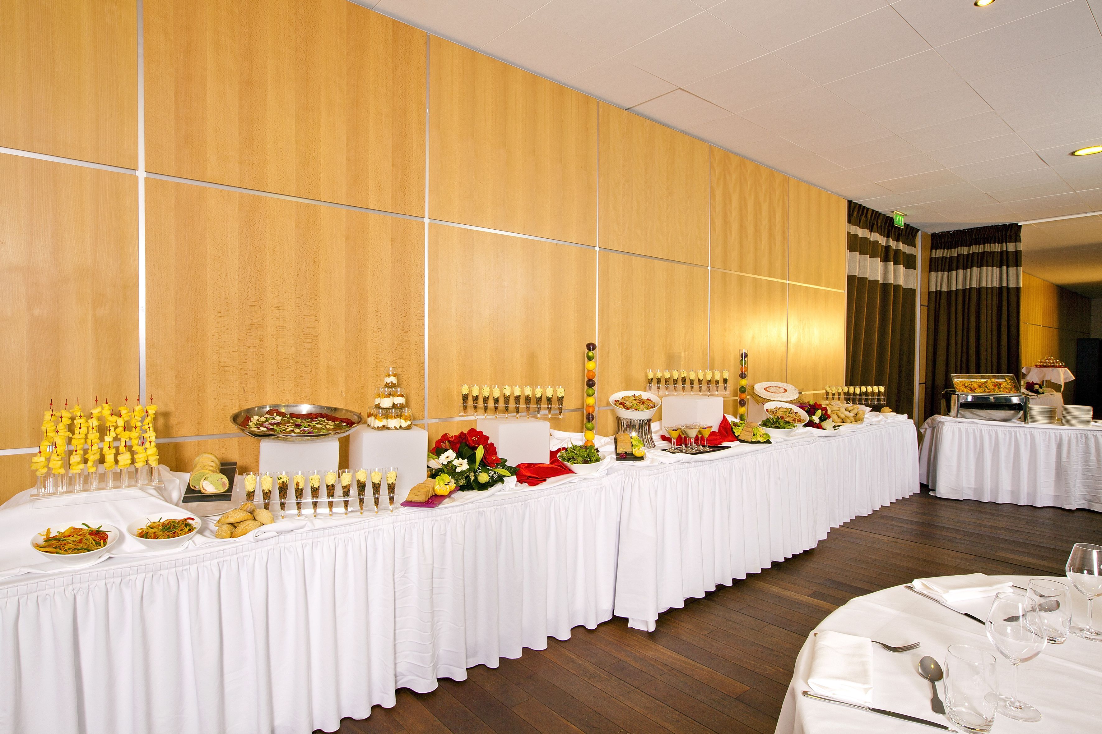 Une salle de banquet avec de longues tables recouvertes de nappes blanches, décorées de plats, de fleurs et de divers éléments de décoration.