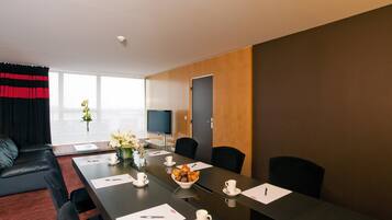A modern conference room with a long table, black chairs, a TV, and a window with curtains.