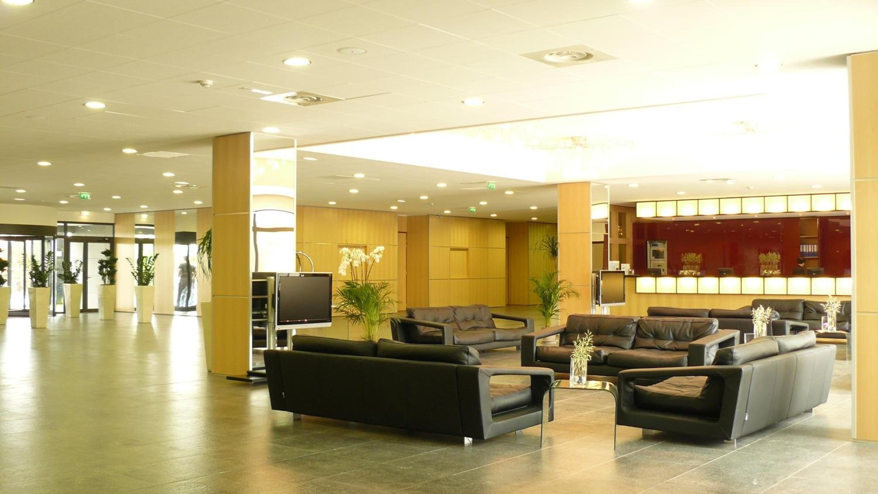 A spacious lobby with modern furniture, a reception desk, and a large screen.