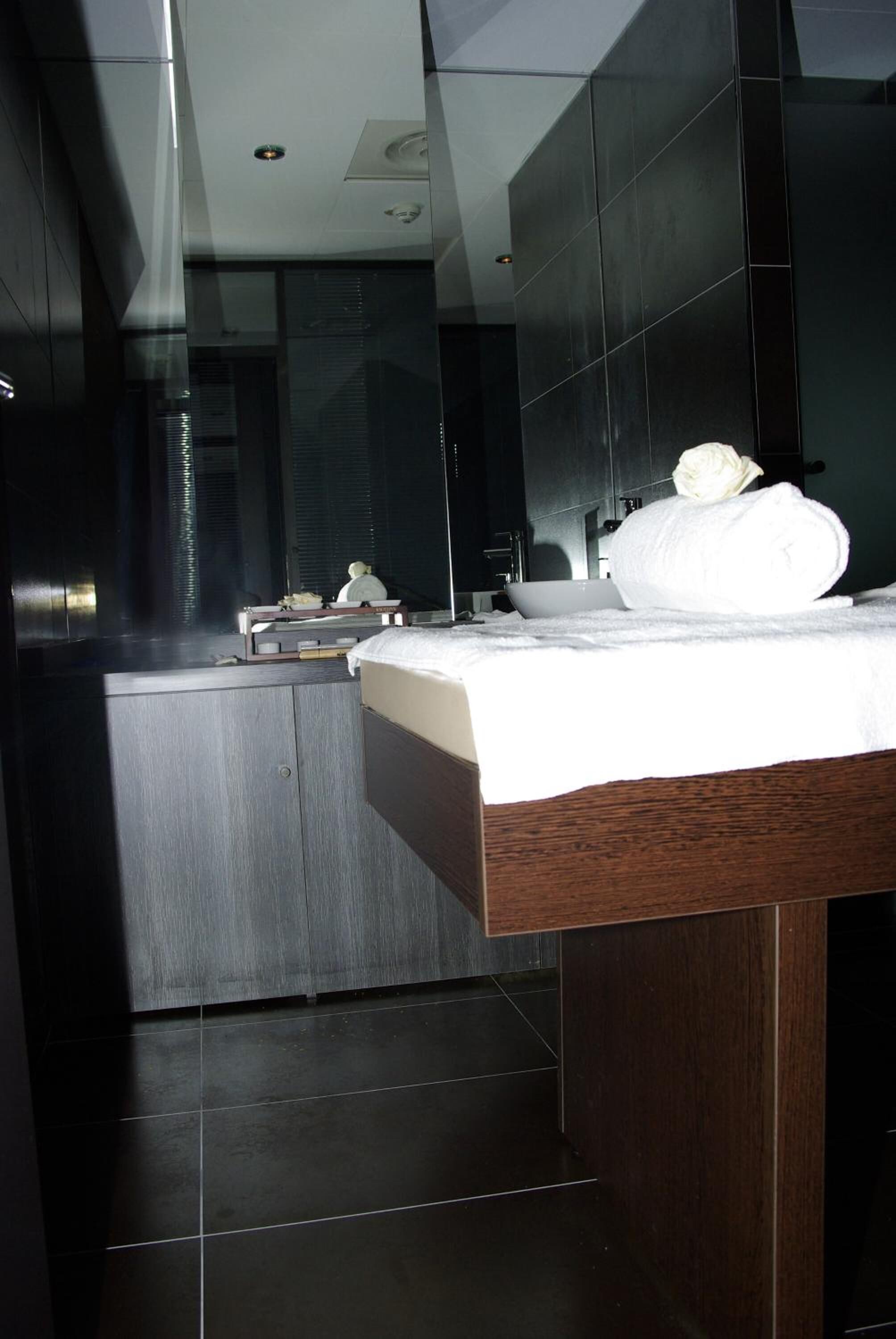 A modern hotel room with a large bed, a bedside table, a mirror, and a small bathroom area.