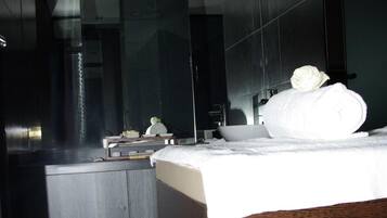 A modern hotel room with a large bed, a bedside table, a mirror, and a small bathroom area.