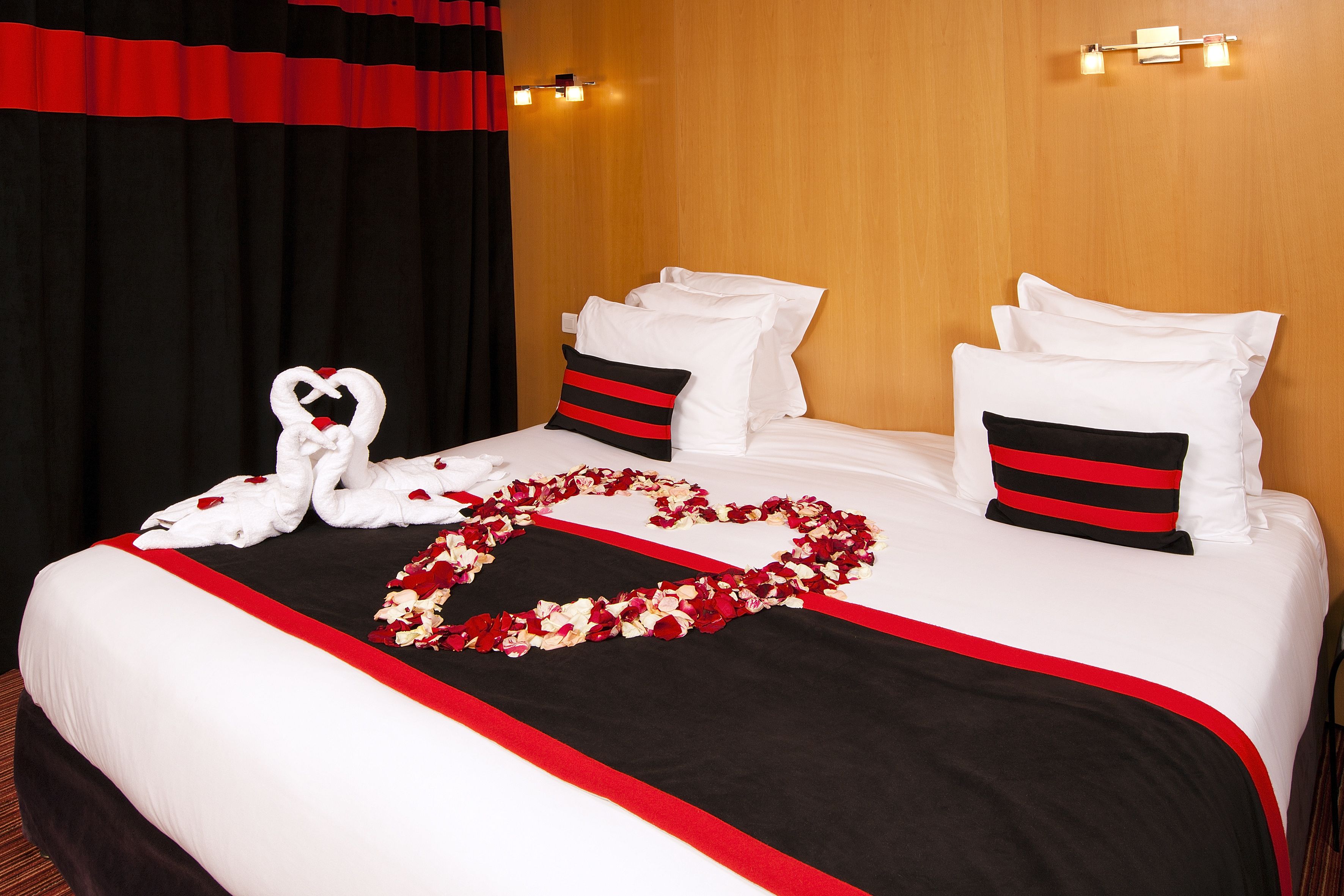 A hotel room with a neatly made bed, a heart-shaped arrangement of rose petals, and a swan-shaped towel decoration.