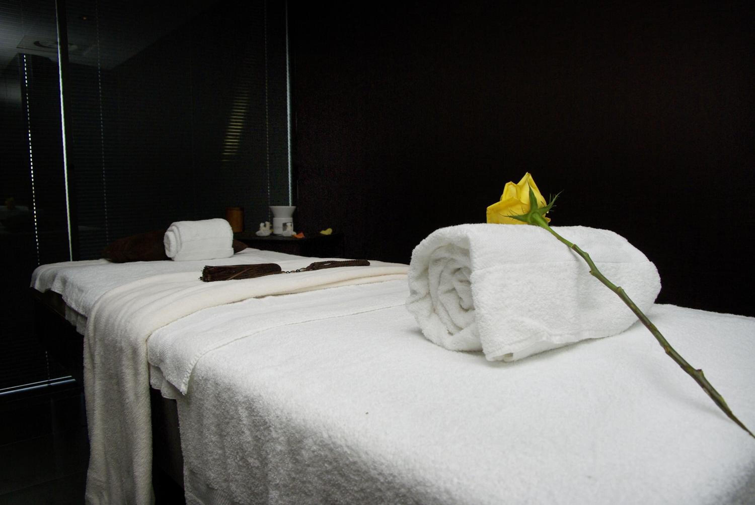 Una cama bien hecha con una toalla blanca y una rosa amarilla.