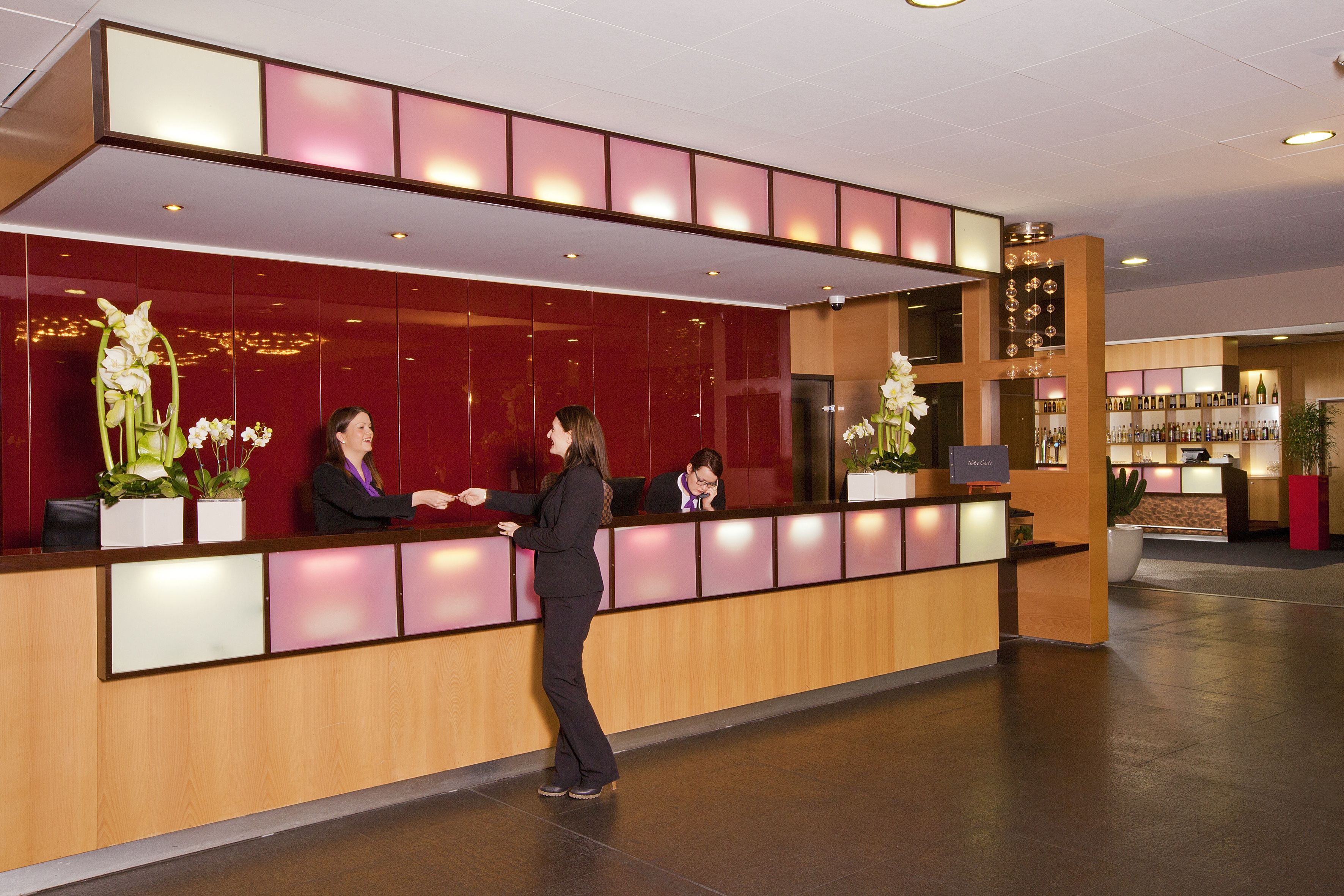 Ett entréområde med en reception i trä, en röd vägg och en bardisk i bakgrunden.