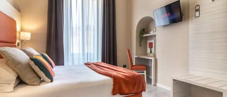 A modern hotel room with a bed, a desk, a TV, and a bench.