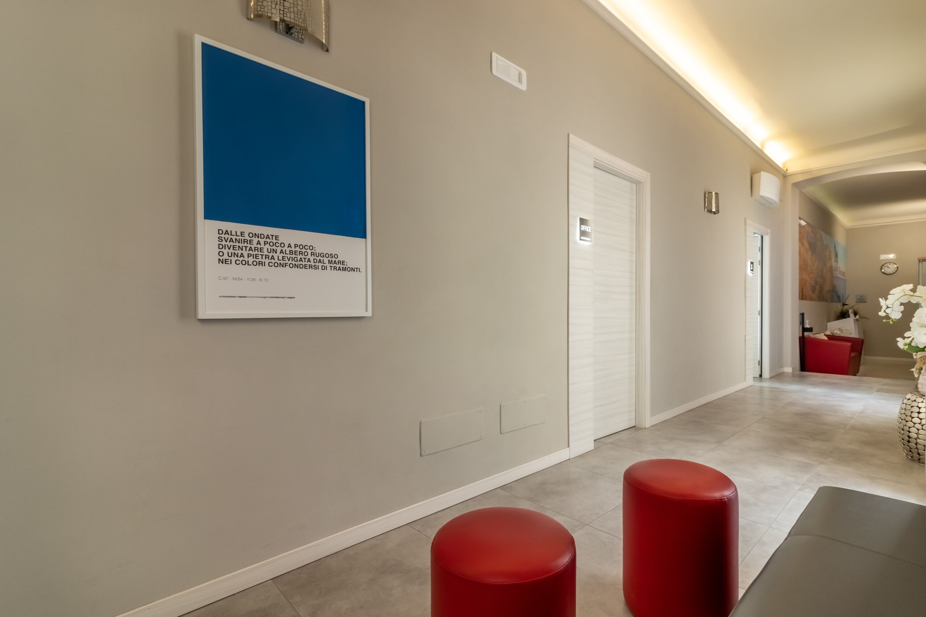 A hallway with a framed artwork, a red stool, and a white door.