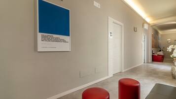 A hallway with a framed artwork, a red stool, and a white door.