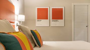 A hotel room with a bed, pillows, a wall-mounted lamp, and two framed artworks.