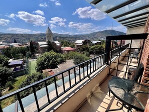 A balcony with a glass table and chairs, overlooking a town with buildings and a church.