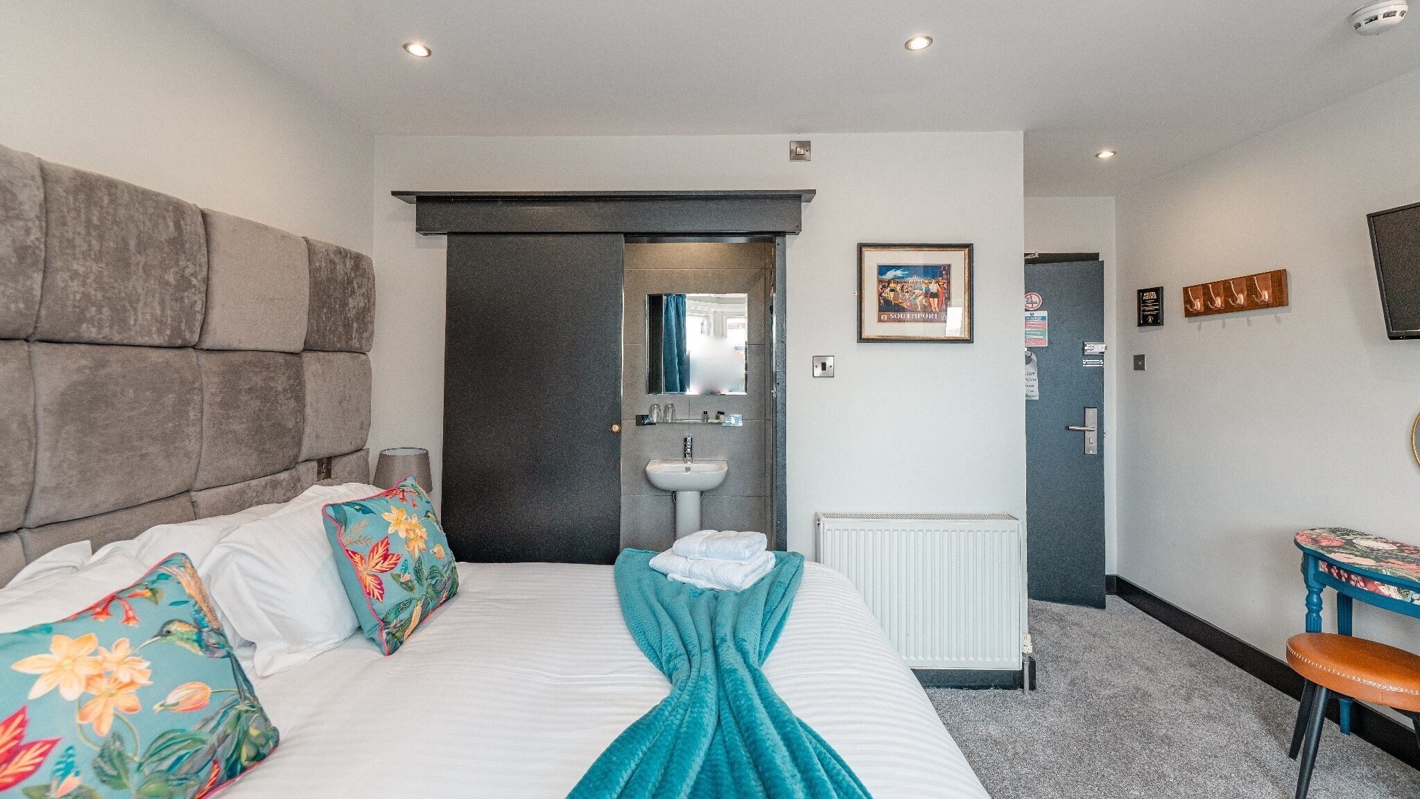 A hotel room with a bed, a bedside table, a chair, a bathroom with a sink, and a door leading to another room.