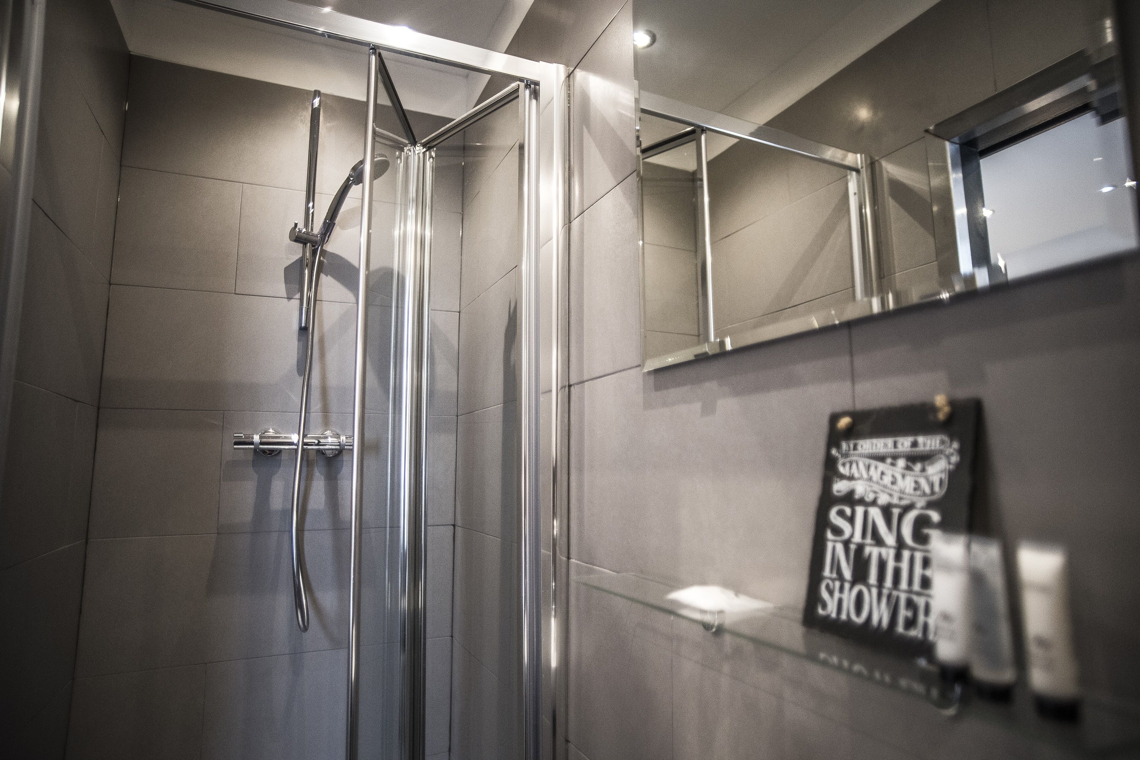 A modern bathroom with a glass shower enclosure, a towel rack, and a sign on the wall.