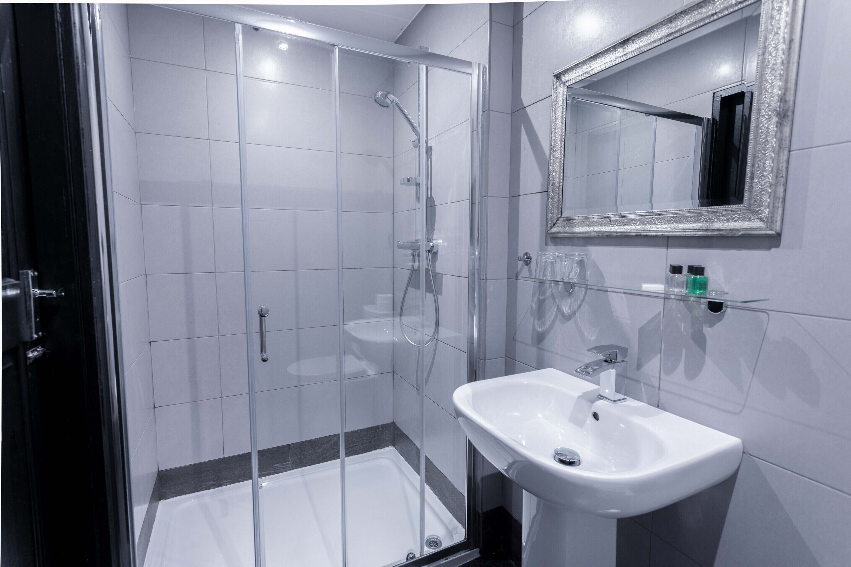 A modern bathroom with a glass shower enclosure, a white sink, and a mirror with an ornate frame.