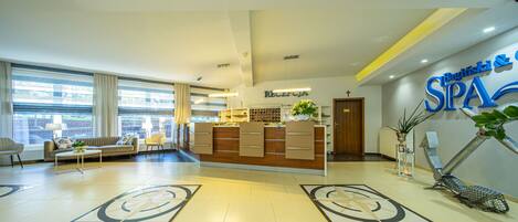 A reception area with a reception desk, a sofa, and a coffee table. There is a reception sign and a wall with a spa sign.