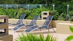 Eine Dachterrasse mit Liegestühlen, einer kleinen Holzkonstruktion und üppigem Grün im Hintergrund.