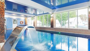 Ein modernes Hallenbad mit Wasserrutsche, großen Fenstern und Blick ins Freie.