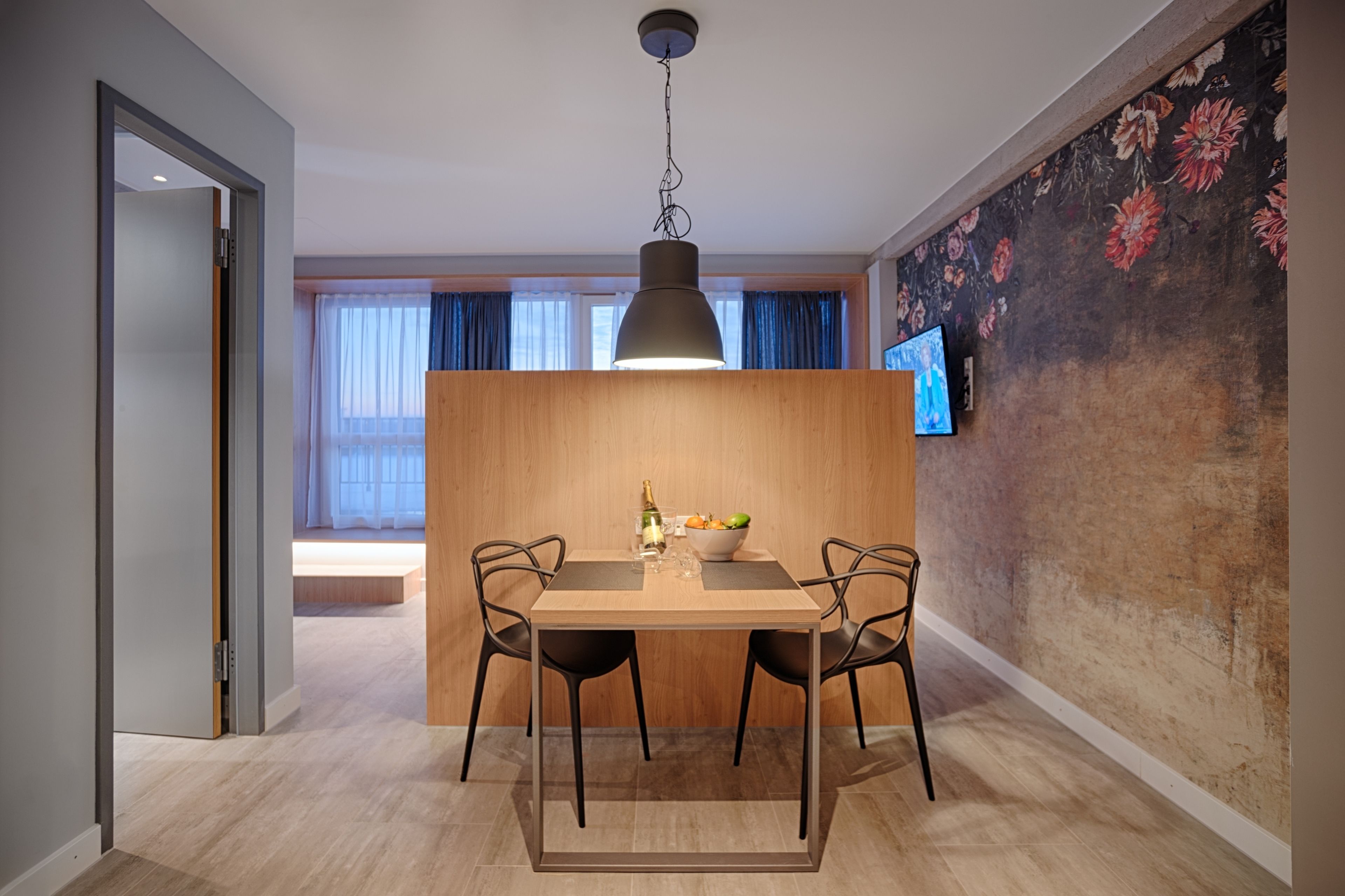 Ein moderner Essbereich mit einem Holztisch, zwei Stühlen, einer Hängeleuchte und einer Wand mit Blumenmuster.