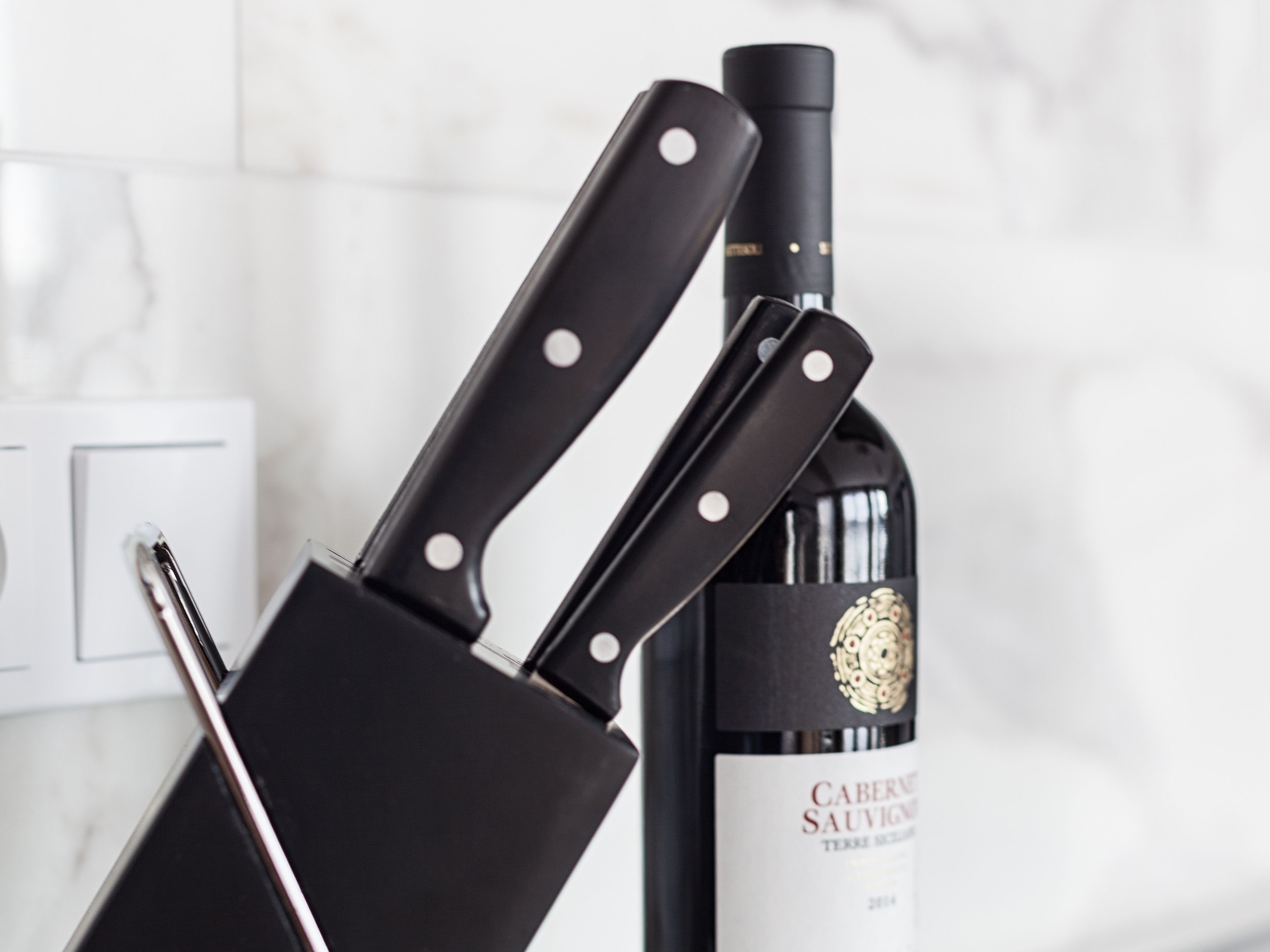 A knife block with two knives and a bottle of wine.