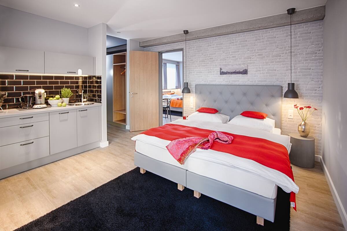 A modern bedroom with a large bed, a separate bathroom, and a kitchen area.