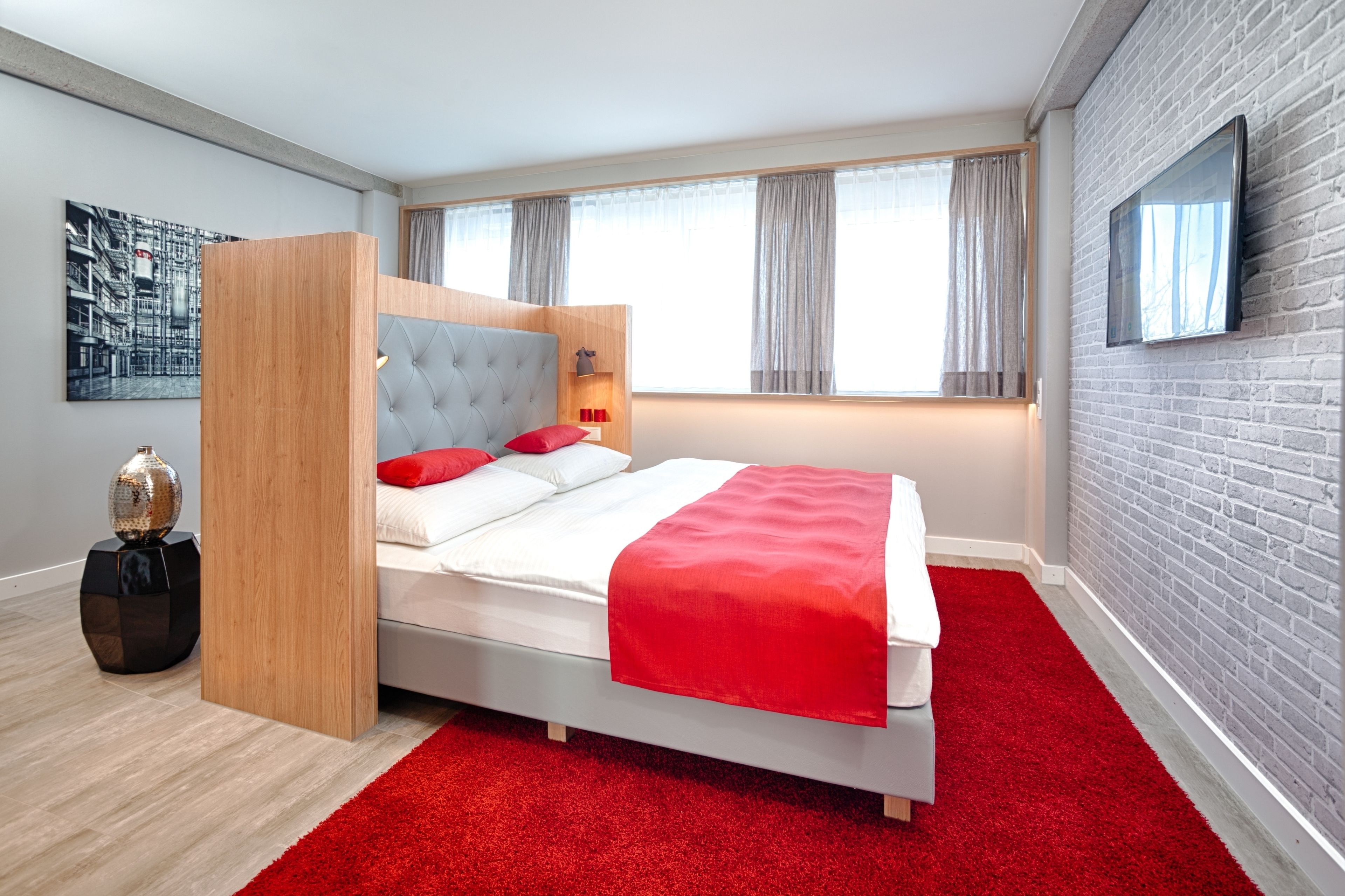 Un dormitorio moderno con cama, alfombra roja, cabecero de madera y pared de ladrillo.