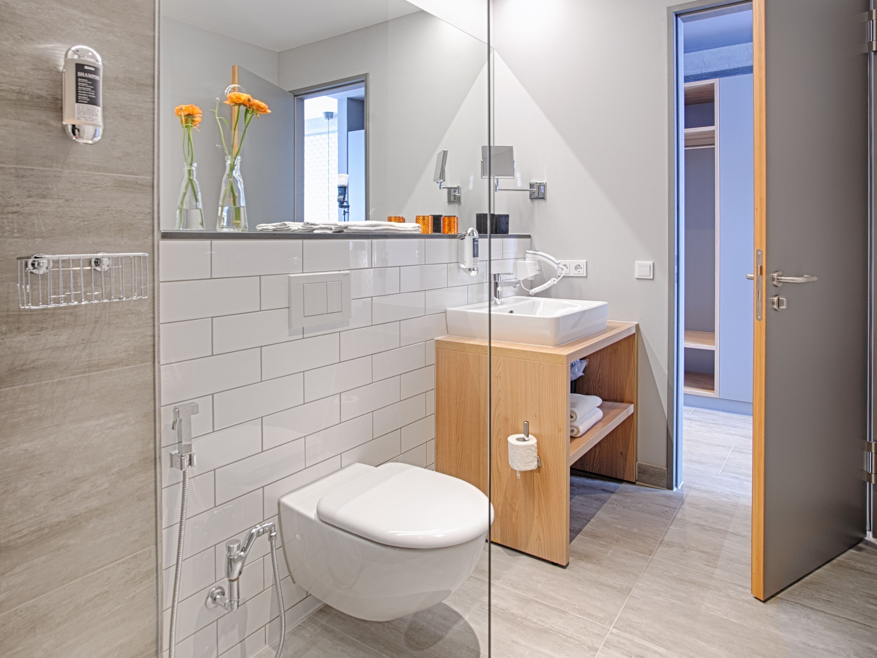 Un baño moderno con cabina de ducha de vidrio, inodoro blanco y tocador de madera con lavabo.