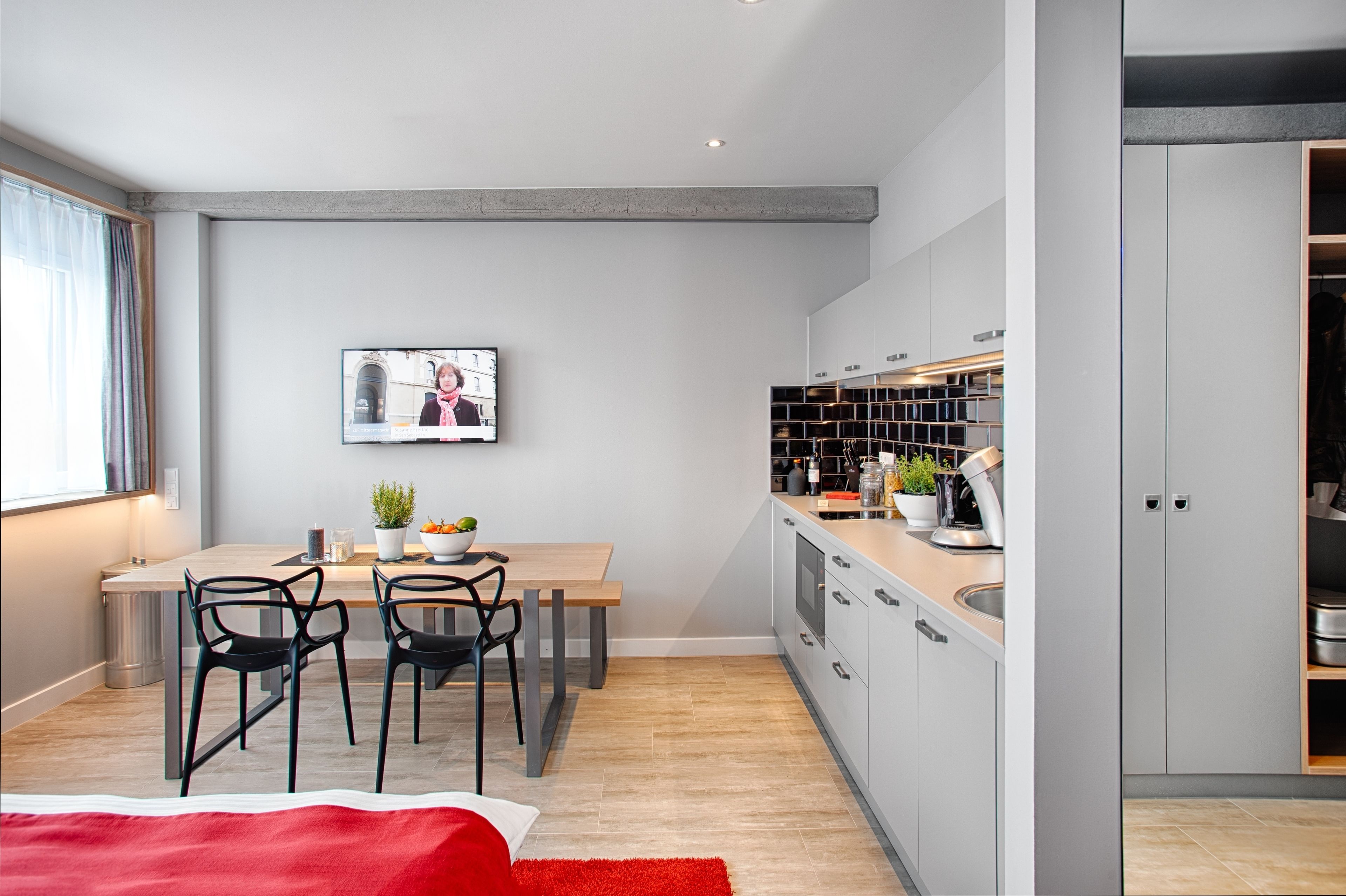 Eine moderne Küche mit Essbereich, ausgestattet mit einem Holztisch, schwarzen Stühlen und einem an der Wand montierten Fernseher.