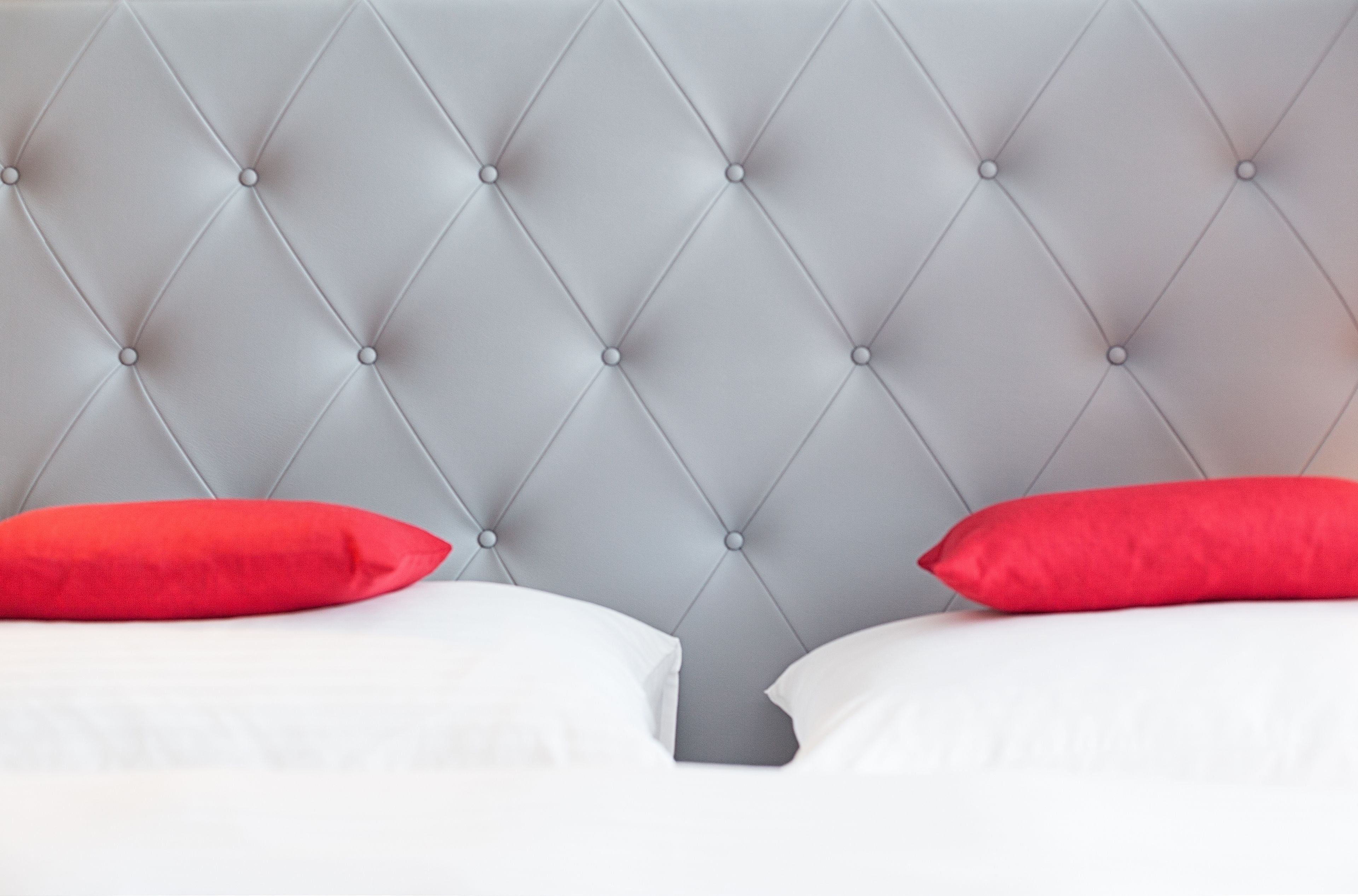 A bed with a tufted headboard and two pillows, one red and one white.