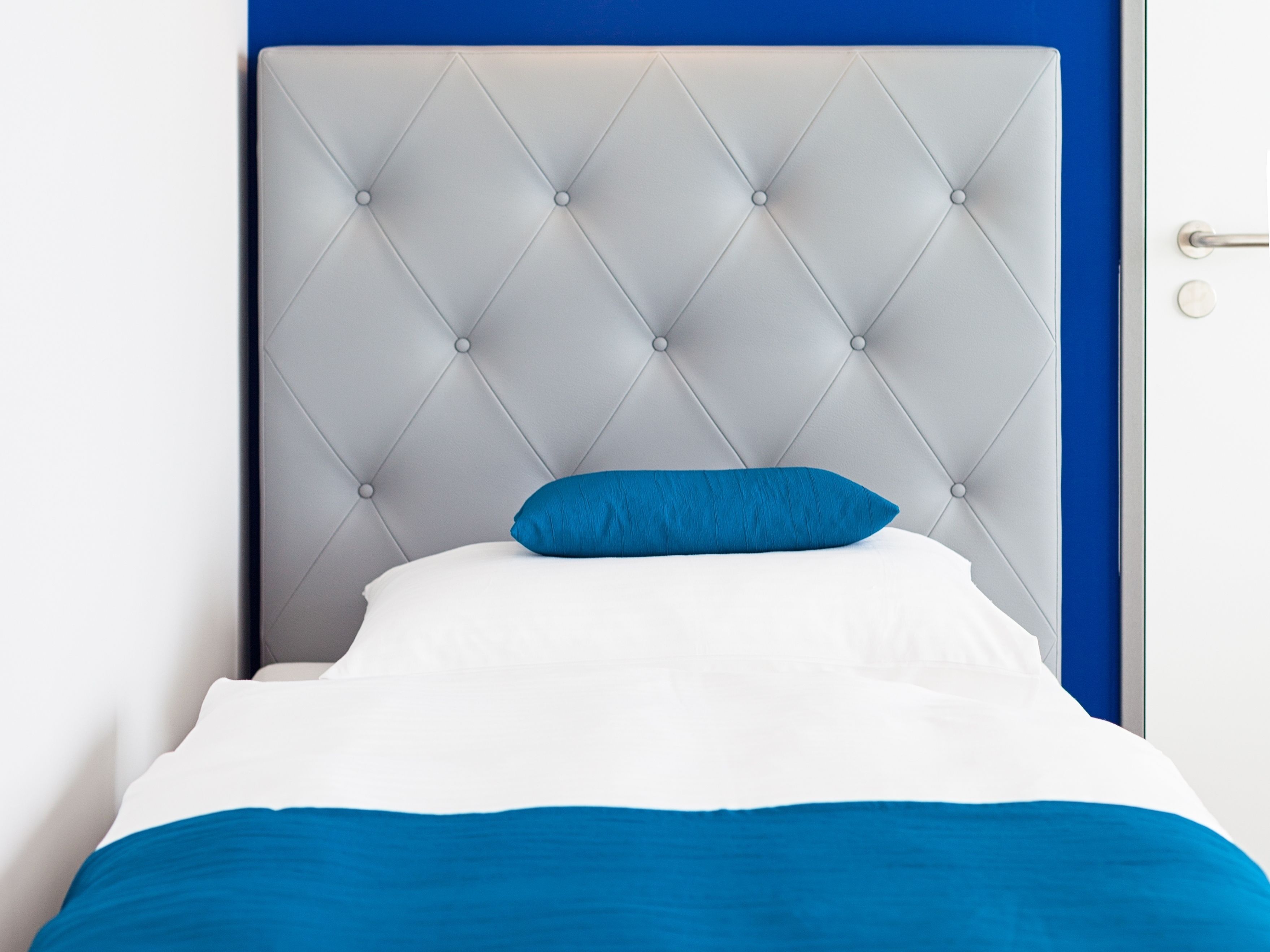 A bed with a tufted headboard, a blue pillow, and white bedding.